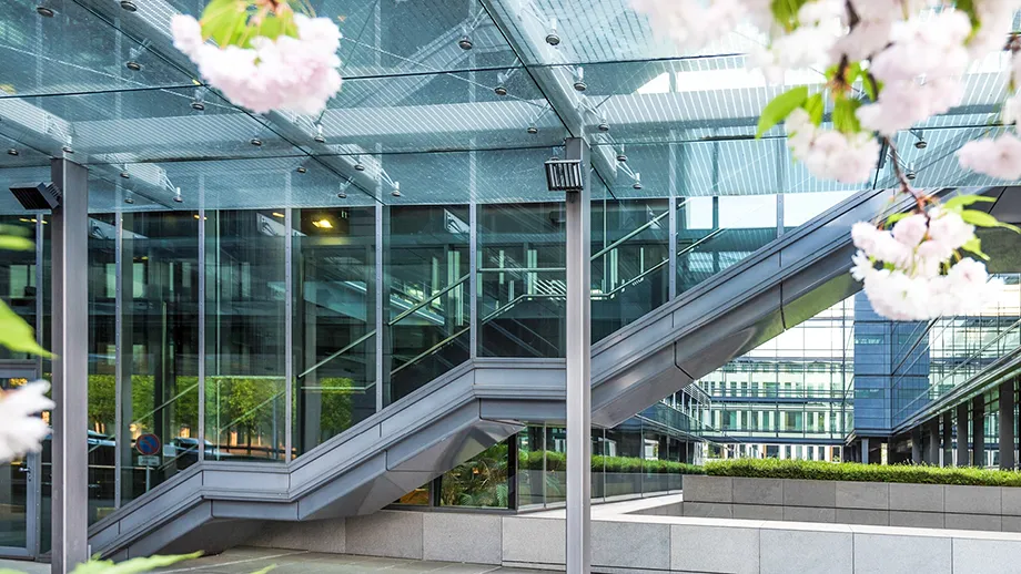 Modern kontorsbyggnad med glasfasad och utomhustrappa, omgiven av blommande träd.