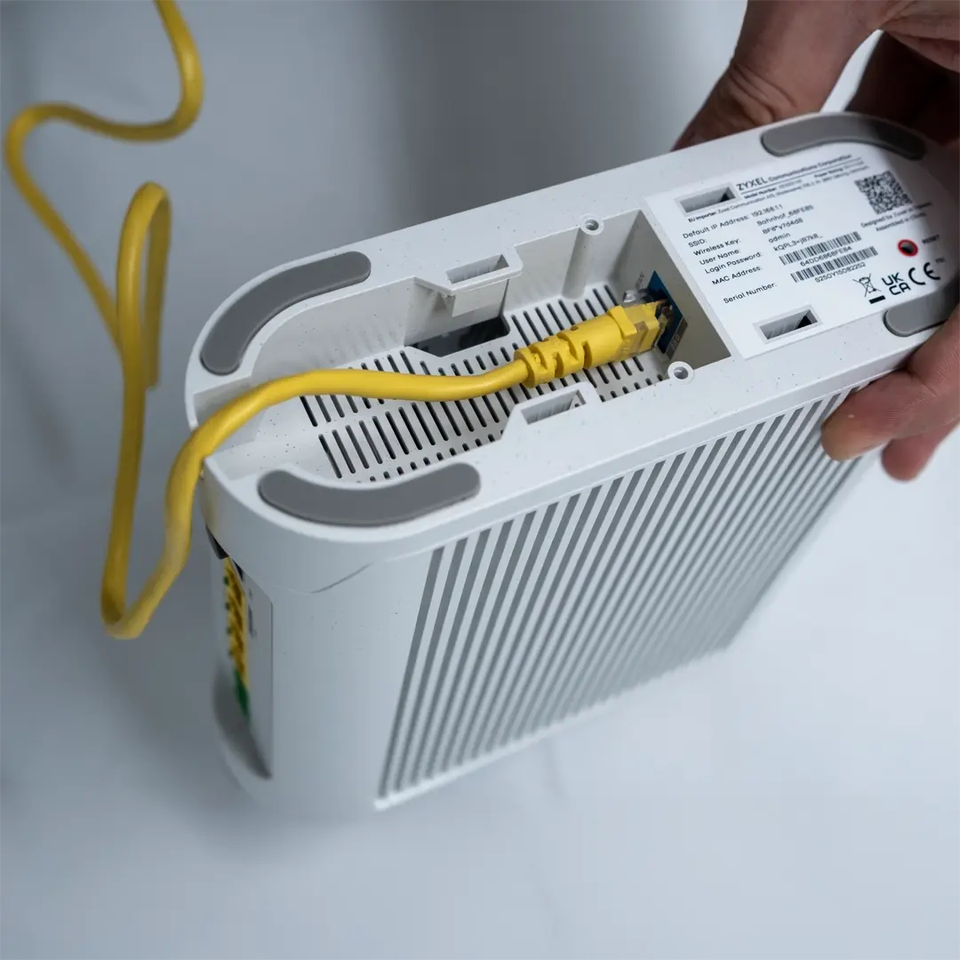 En person håller i en Zyxel-router och har anslutit en gul nätverkskabel till porten på undersidan av enheten.