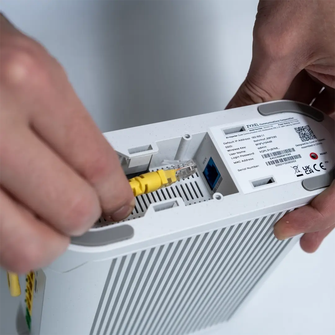 En person ansluter en gul nätverkskabel till porten på undersidan av en router från Zyxel.