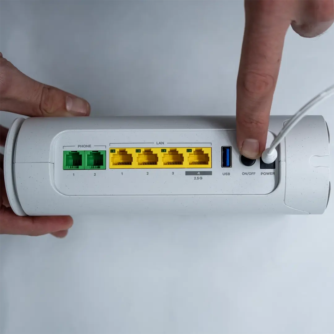 En person trycker på strömknappen på baksidan av en Zyxel-router för att starta den. Strömkabeln är ansluten, och de gula LAN-portarna samt USB-porten syns tydligt.