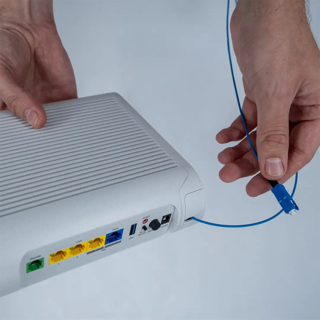 En person håller i en router och visar den blå fiberkabeln som ska kopplas till fiberuttaget i bostaden.