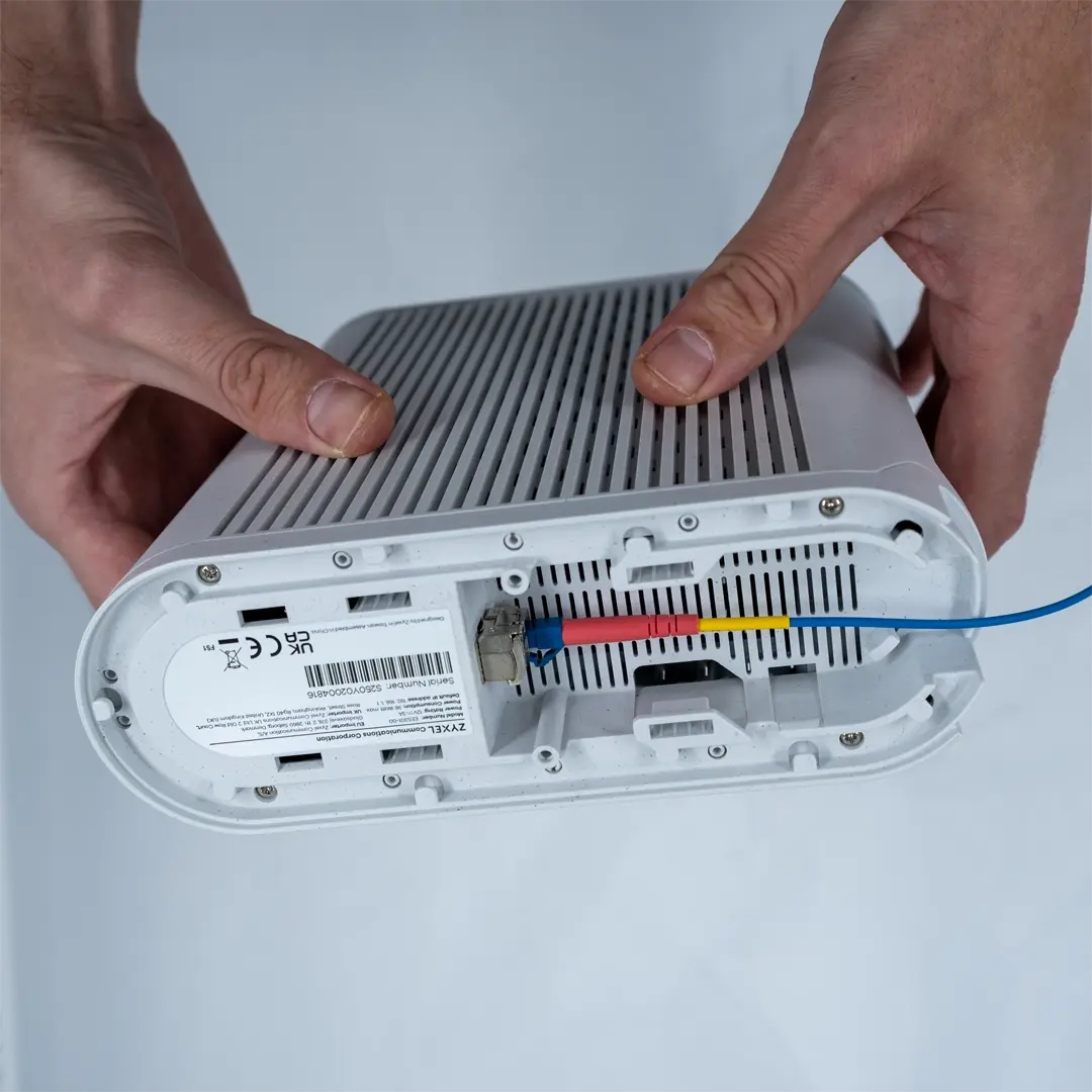 En person håller i en router upp och ned och visar hur en SFP-modul med ansluten blå fiberkabel är isatt i uttaget på undersidan av enheten.