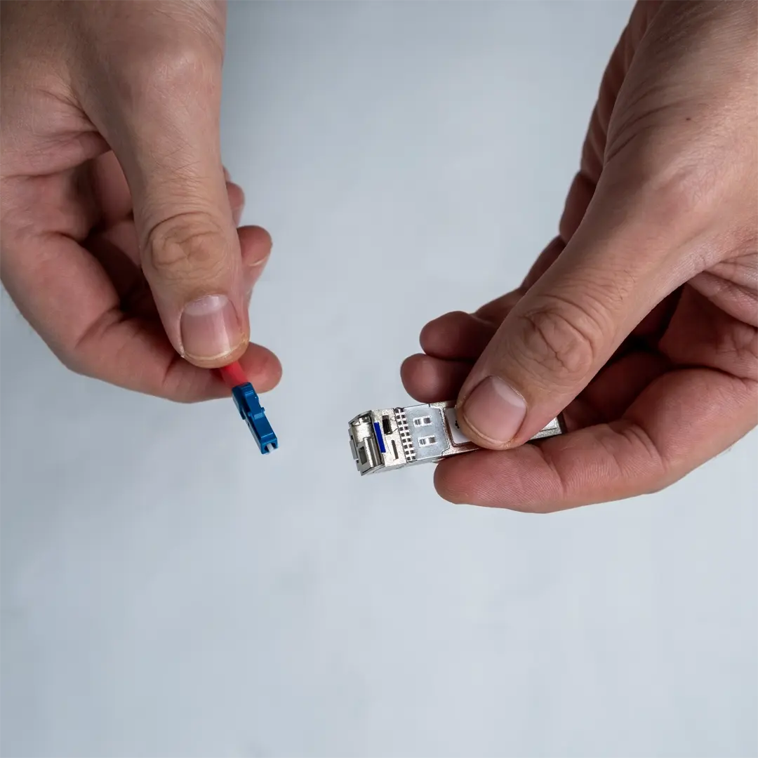 En person håller en SFP-modul i ena handen och visar den blå fiberkabelns kontakt i den andra.