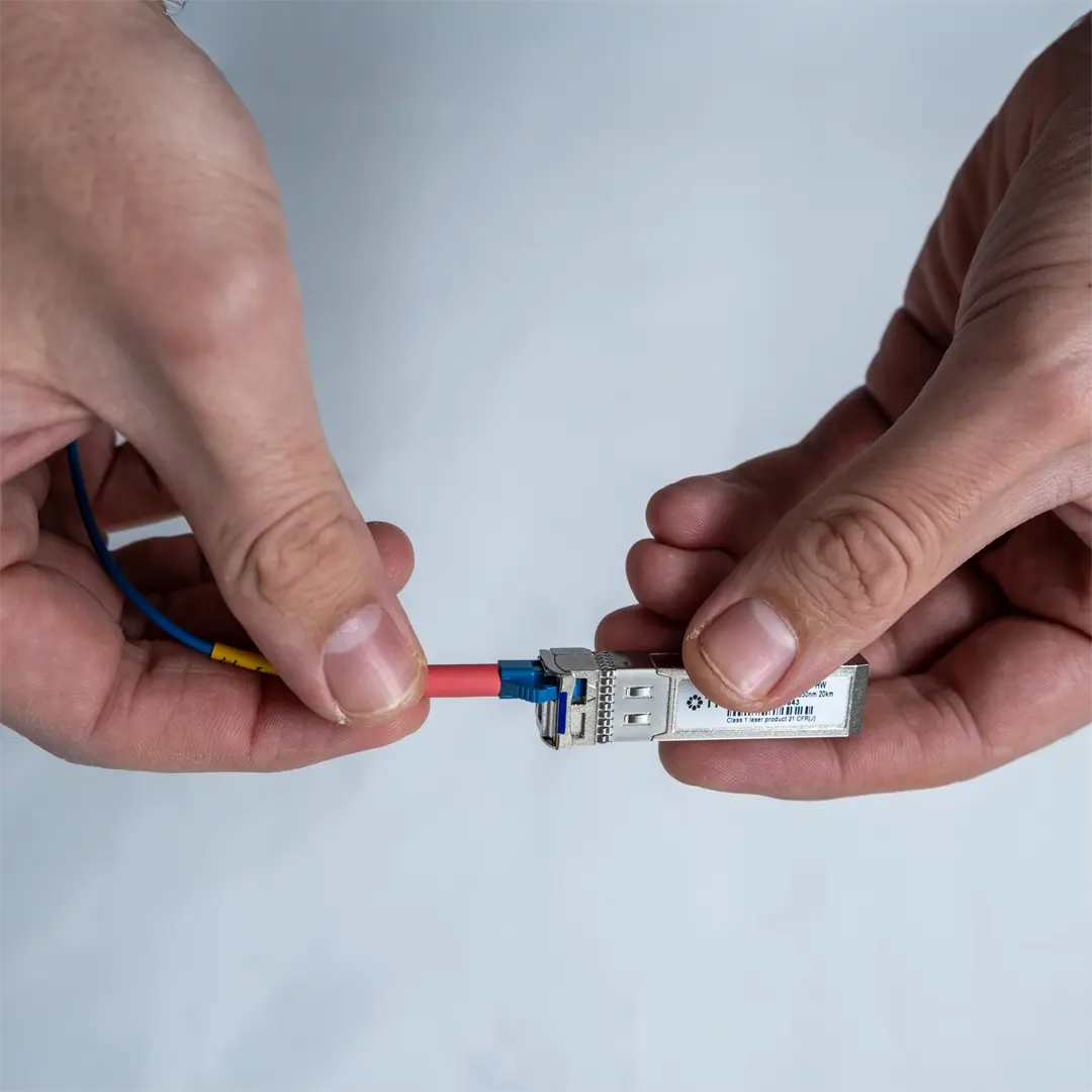 En person ansluter en blå fiberkabel till en SFP-modul genom att försiktigt föra in kontakten tills den sitter fast.