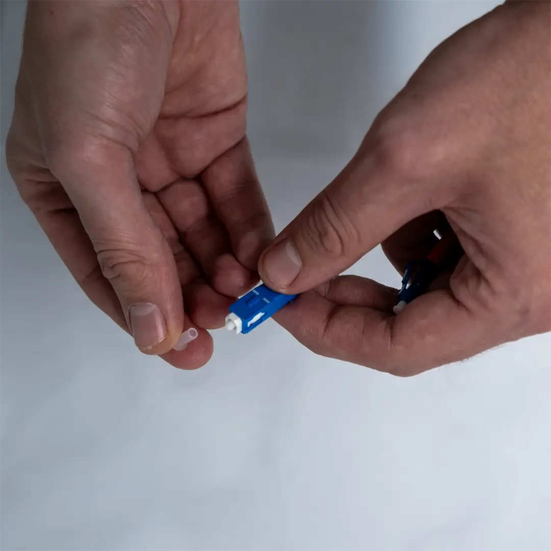 En person tar bort den genomskinliga skyddskåpan från änden av en blå fiberkabel.