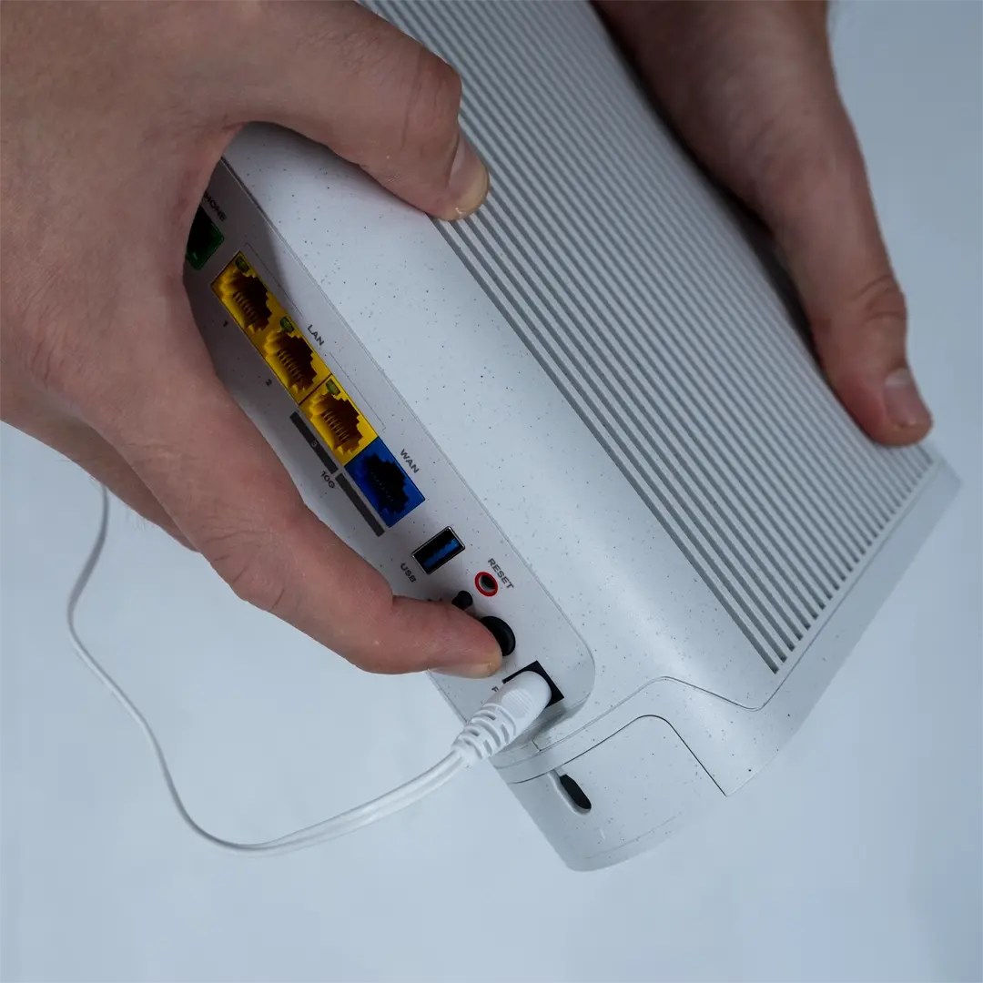 En person trycker på strömknappen på baksidan av en router efter att ha anslutit strömkabeln till uttaget.
