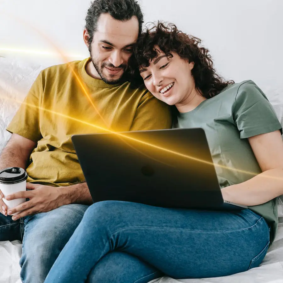 Par sitter i soffan med laptop och kaffe.