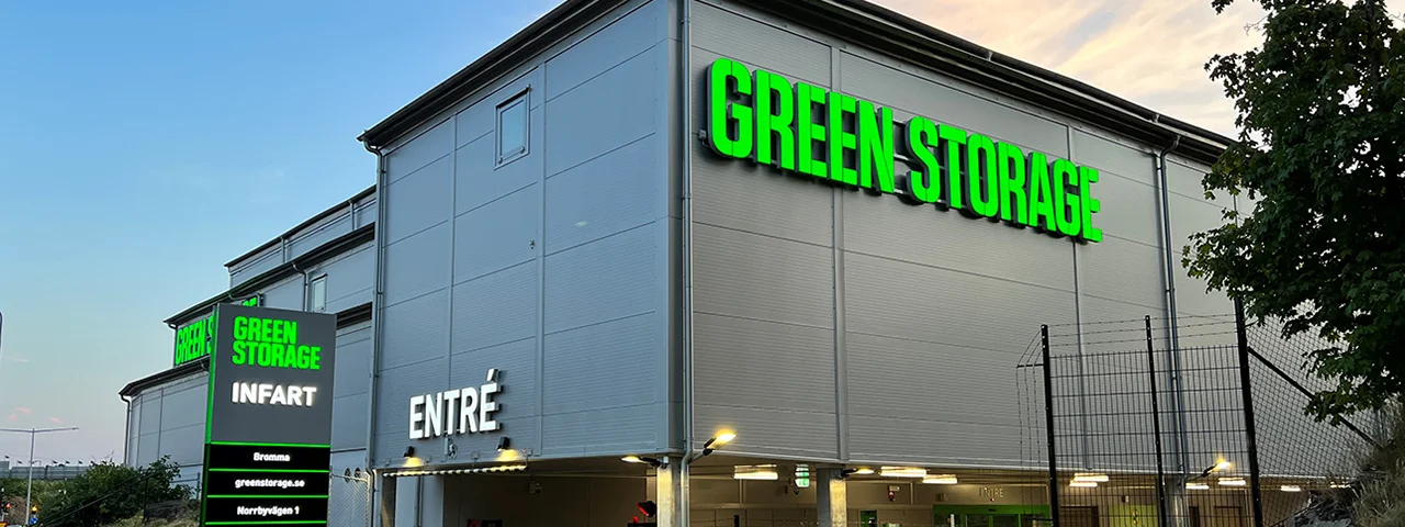 Fasad med stor grön skylt med texten Green Storage på en modern industribyggnad under dagsljus.
