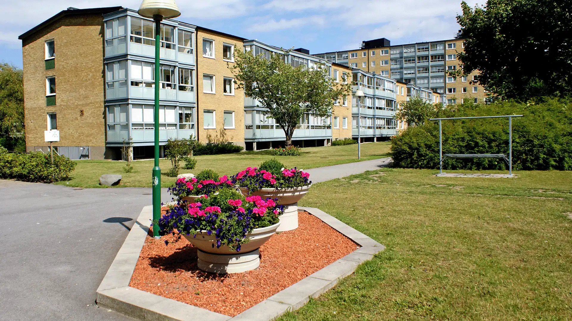 Flerbostadshus i bostadsrättsföreningen BRF Domaren i Malmö med grön innergård, gångvägar och blomplanteringar en solig dag.