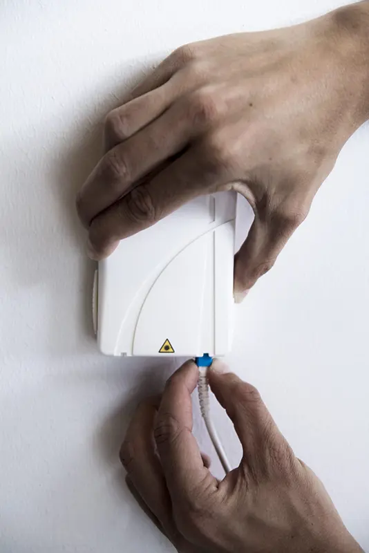 Händer som för in blå fiberkontakt i fiberuttag på vägg.