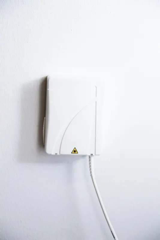 Fiberuttag monterat på vit vägg med fiberkabel ansluten undertill.