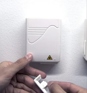 Hand som tar bort plasthållare från fiberuttag på väggen.