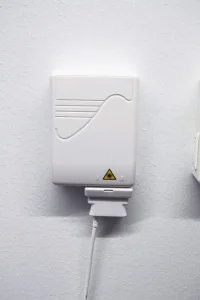 Fiberuttag monterat på vit vägg med vågformad front och fiberkabel ansluten via plasthållare undertill.