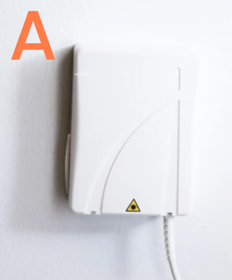 Fiberuttag modell A monterat på vit vägg, med lasersymbol längst ned och fiberkabel ansluten undertill.