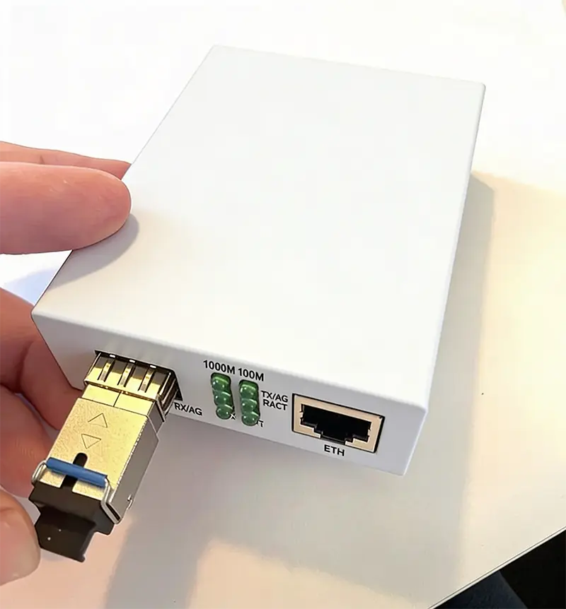Närbild på vit mediakonverter med insatt SFP-modul i metall på vänster sida, LED-indikatorer på framsidan och nätverksuttag (RJ45) till höger, hålls i en hand mot ljus bakgrund.