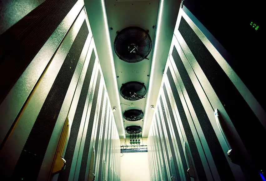 Serverhall i Bahnhofs datacenter St Erik i Stockholm. Bilden visar en smal gång mellan höga serverrack med kylfläktar i taket, belyst av grönt och vitt ljus som framhäver den tekniska och futuristiska miljön.