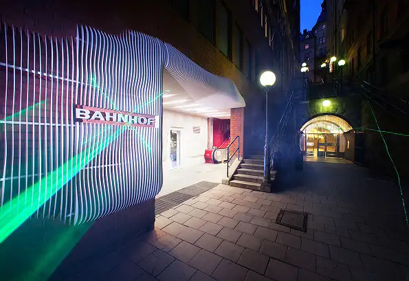 Ingången till Bahnhofs datacenter Thule i Stockholm vid skymning. Fasaden är upplyst med böjda vita linjer och gröna laserljus, och Bahnhofs logotyp syns tydligt på väggen till vänster.